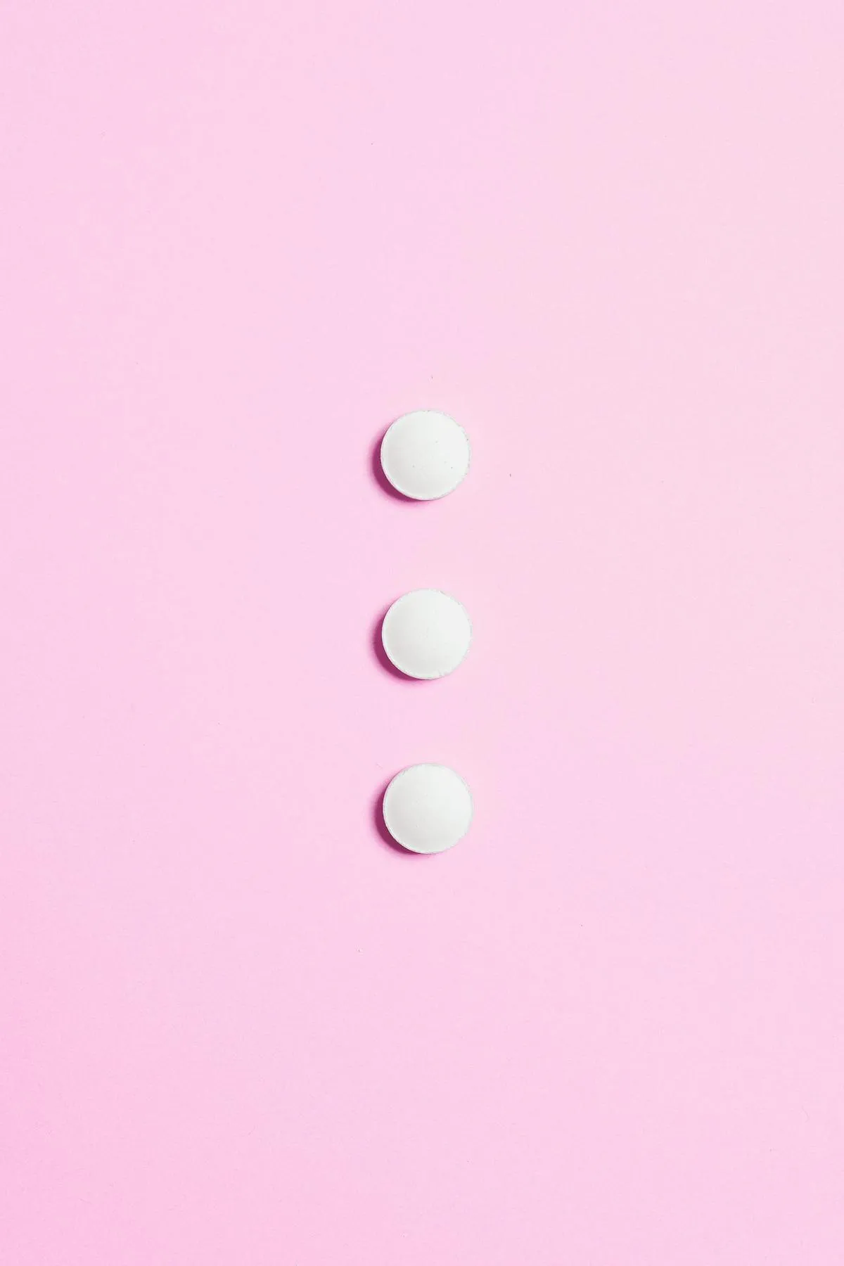 A minimalist composition featuring three white pills on a vibrant pink background.